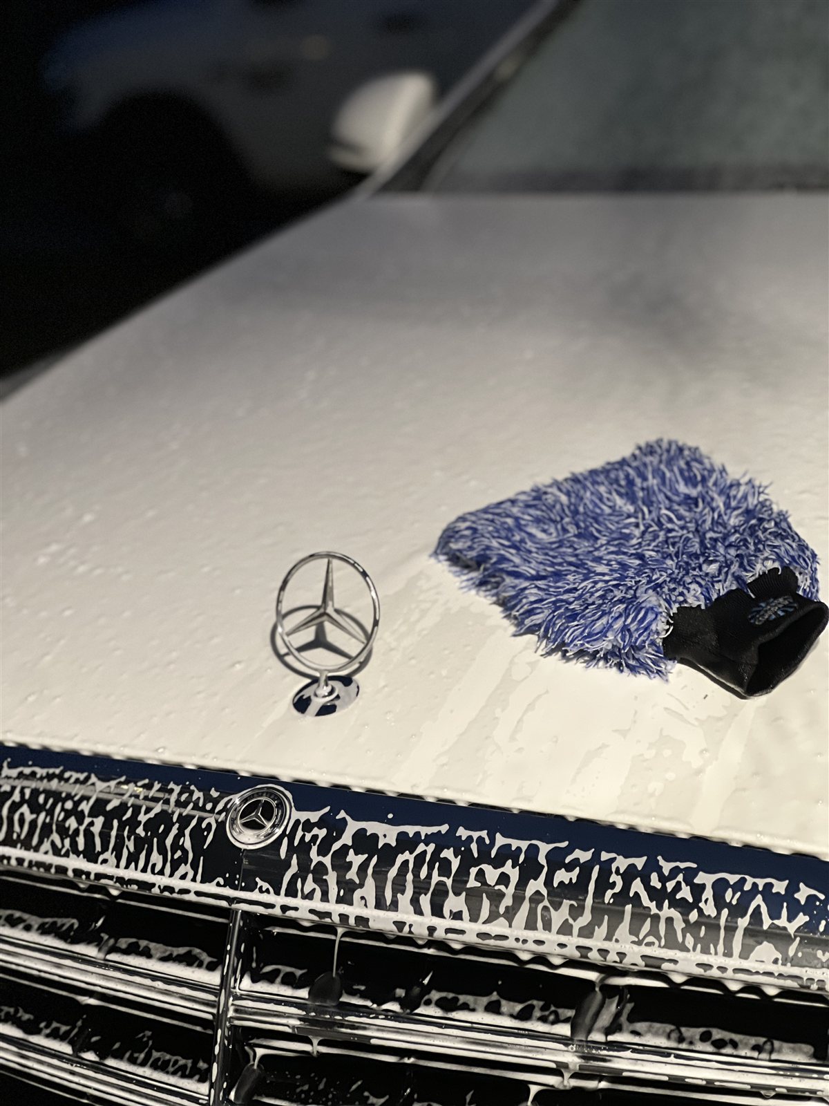 Foam and a wash mitt on the hood of a white Mercedes during a hand wash